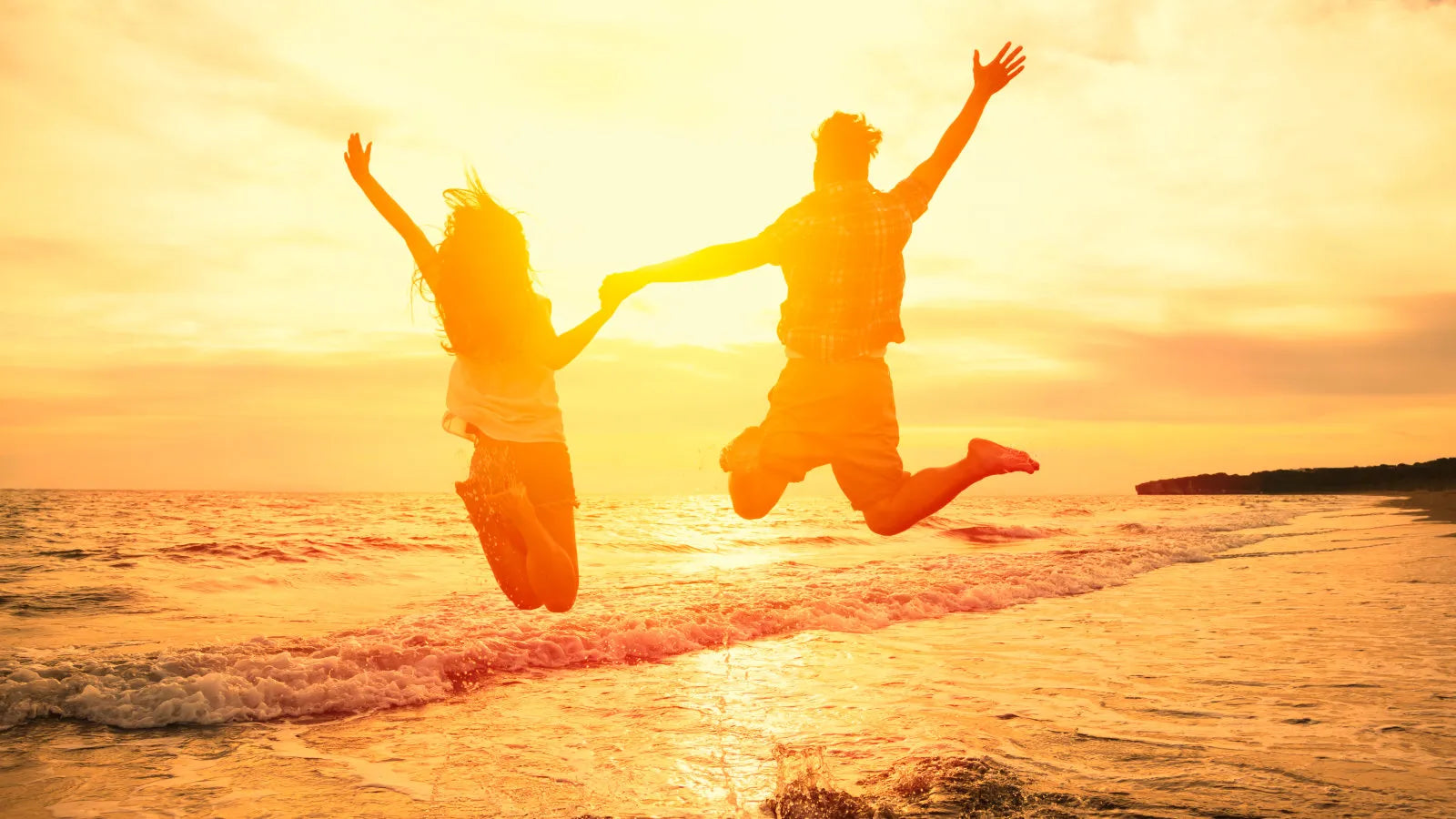 Paar springt freudig in die Luft vor Sonnenuntergang am Meer – Symbol für Leichtigkeit und Lebensfreude