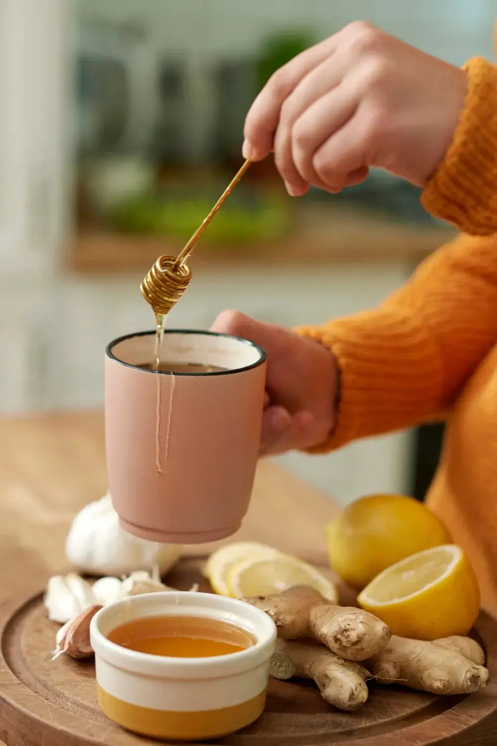 Frau bereitet Tee zu – Fokus auf Löffel mit Honig über einer Tasse, im Hintergrund Zitronen