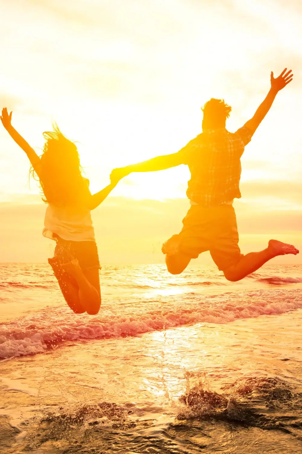 Paar springt fröhlich in die Luft am Meer bei Sonnenuntergang.