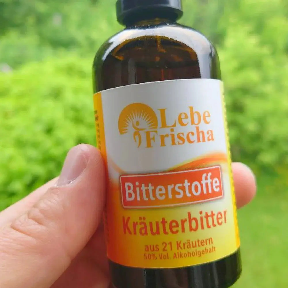 Hand hält eine Bitterstoffe Flasche der Marke LebeFrischa vor grünen Rasen.