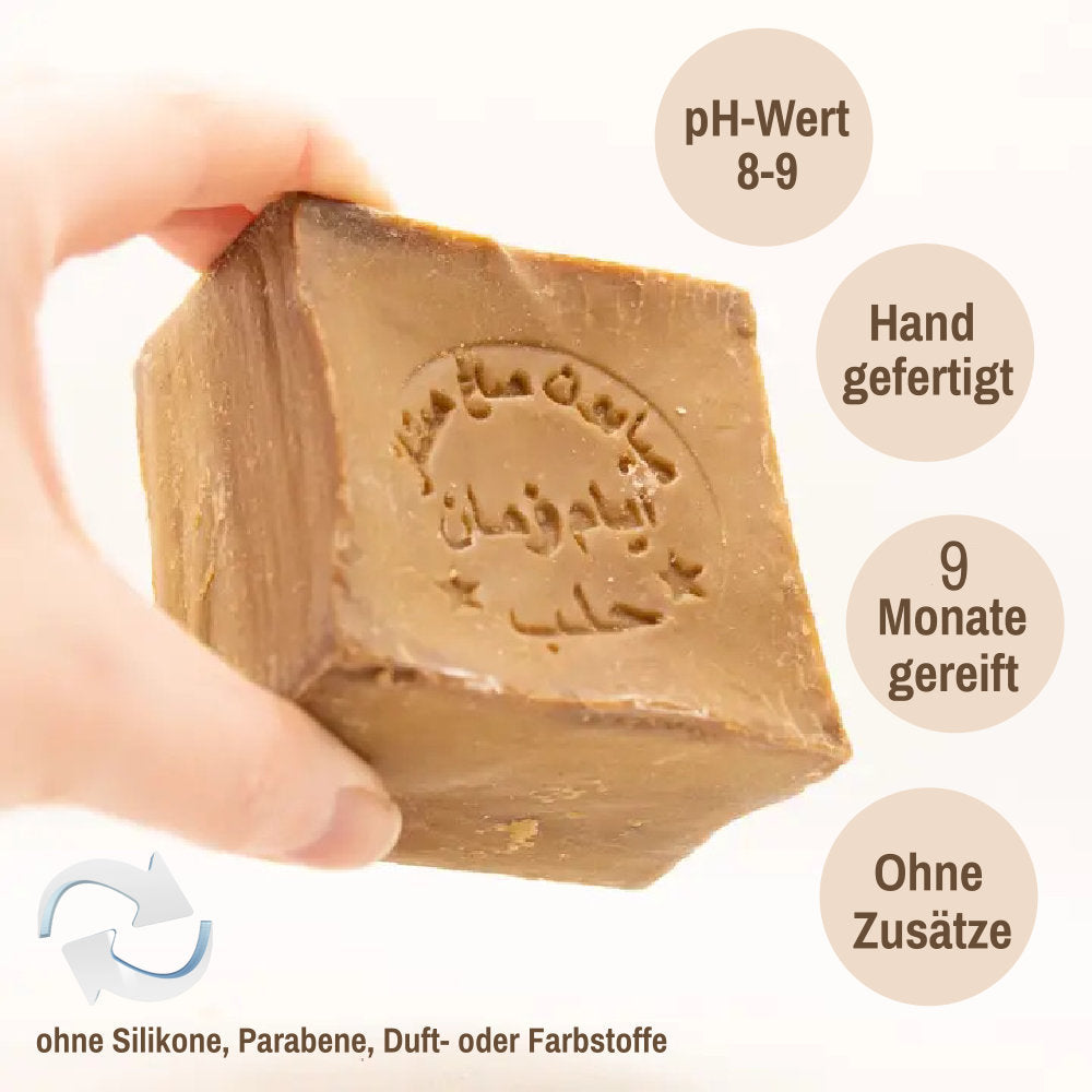 Hand, die eine Aleppo Seife mit geprägter arabischer Schrift hält; daneben sichtbare Texte „pH-Wert 8–9“, „Hand gefertigt“, „9 Monate gereift“, „Ohne Zusätze“ sowie unten „ohne Silikone, Parabene, Duft- oder Farbstoffe“.