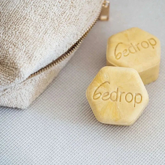 Mehrere Sechseckige gelbe Seifenblöcke mit dem sichtbaren Schriftzug bedrop neben einer Badetasche.